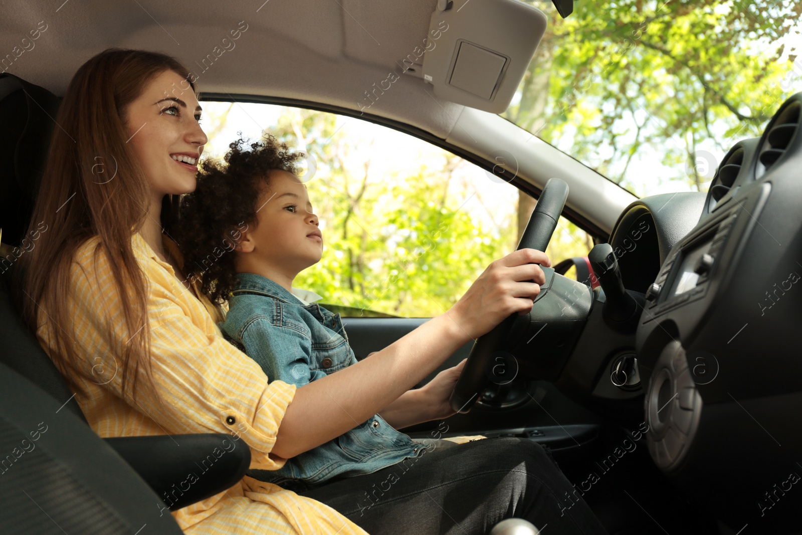 Photo of Mother with cute little daughter driving car together. Child in danger