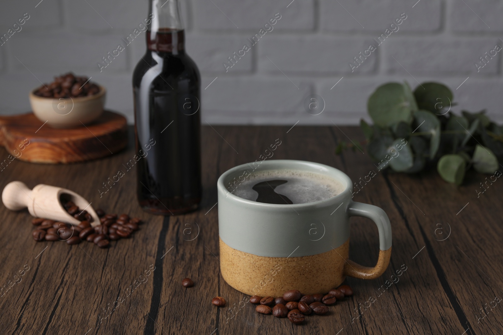 Photo of Mug of aromatic coffee, syrup and beans on wooden table