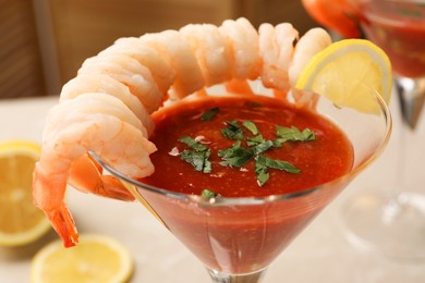 Tasty shrimp cocktail with sauce in glass and lemon on white table, closeup