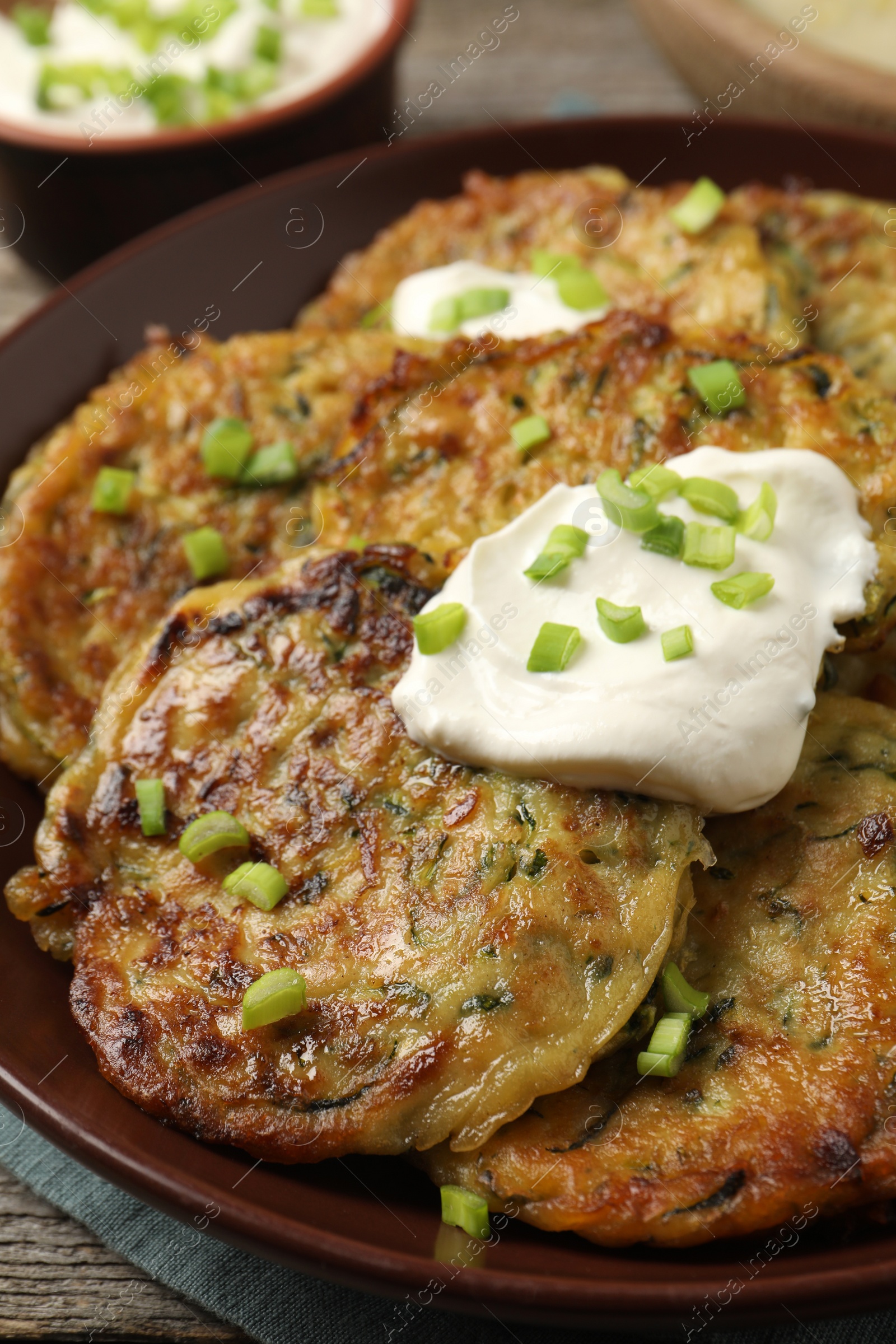 Photo of Delicious zucchini pancakes with sour cream and green onion on table, closeup