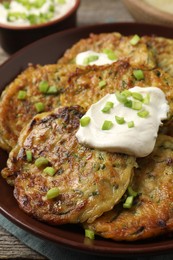 Photo of Delicious zucchini pancakes with sour cream and green onion on table, closeup