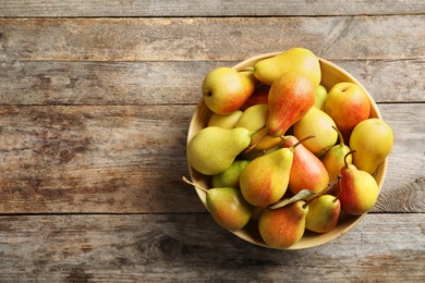 Photo of Bowl with ripe pears on wooden background, top view. Space for text