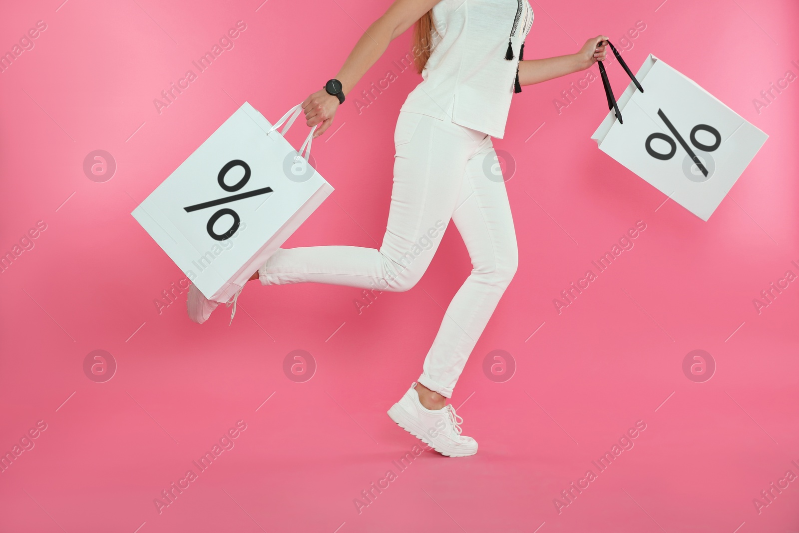 Image of Discount, sale, offer. Woman running with shopping bags against pink background, closeup. Paper bags with percent signs