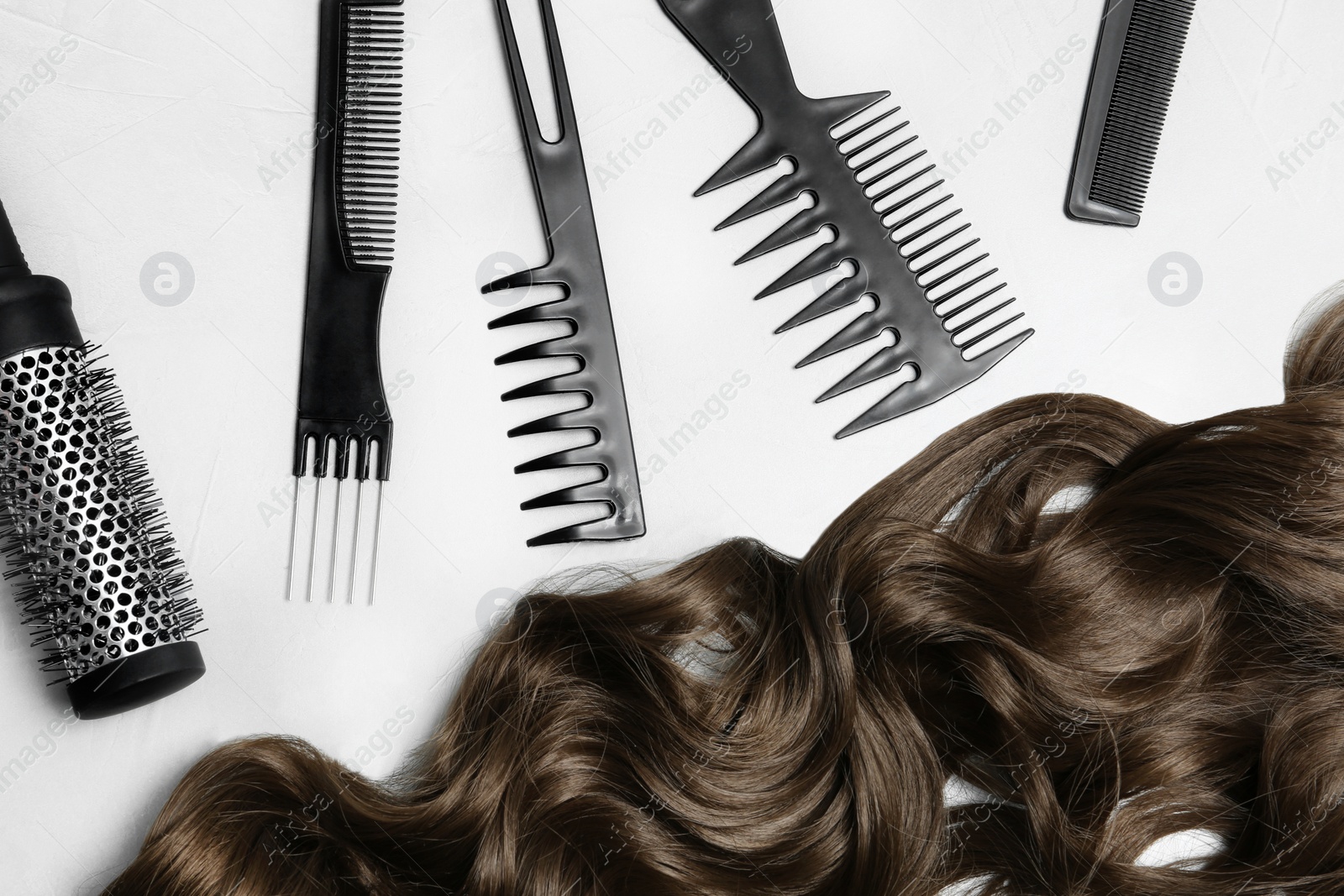 Photo of Flat lay composition with brown hair and hairdresser's tools on light background