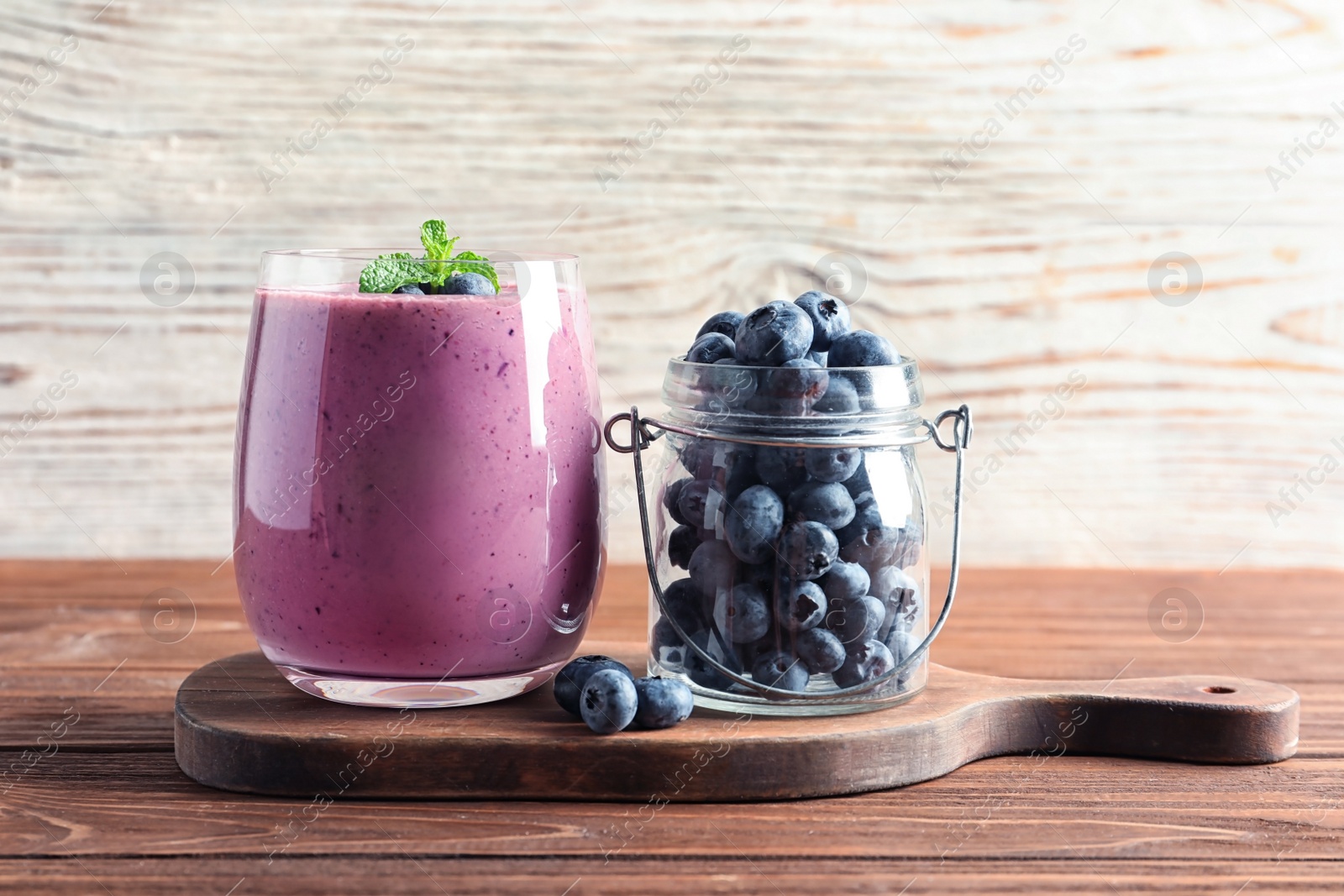 Photo of Glass of smoothie and jar with blueberries on wooden table