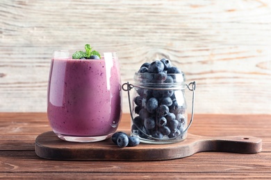 Glass of smoothie and jar with blueberries on wooden table