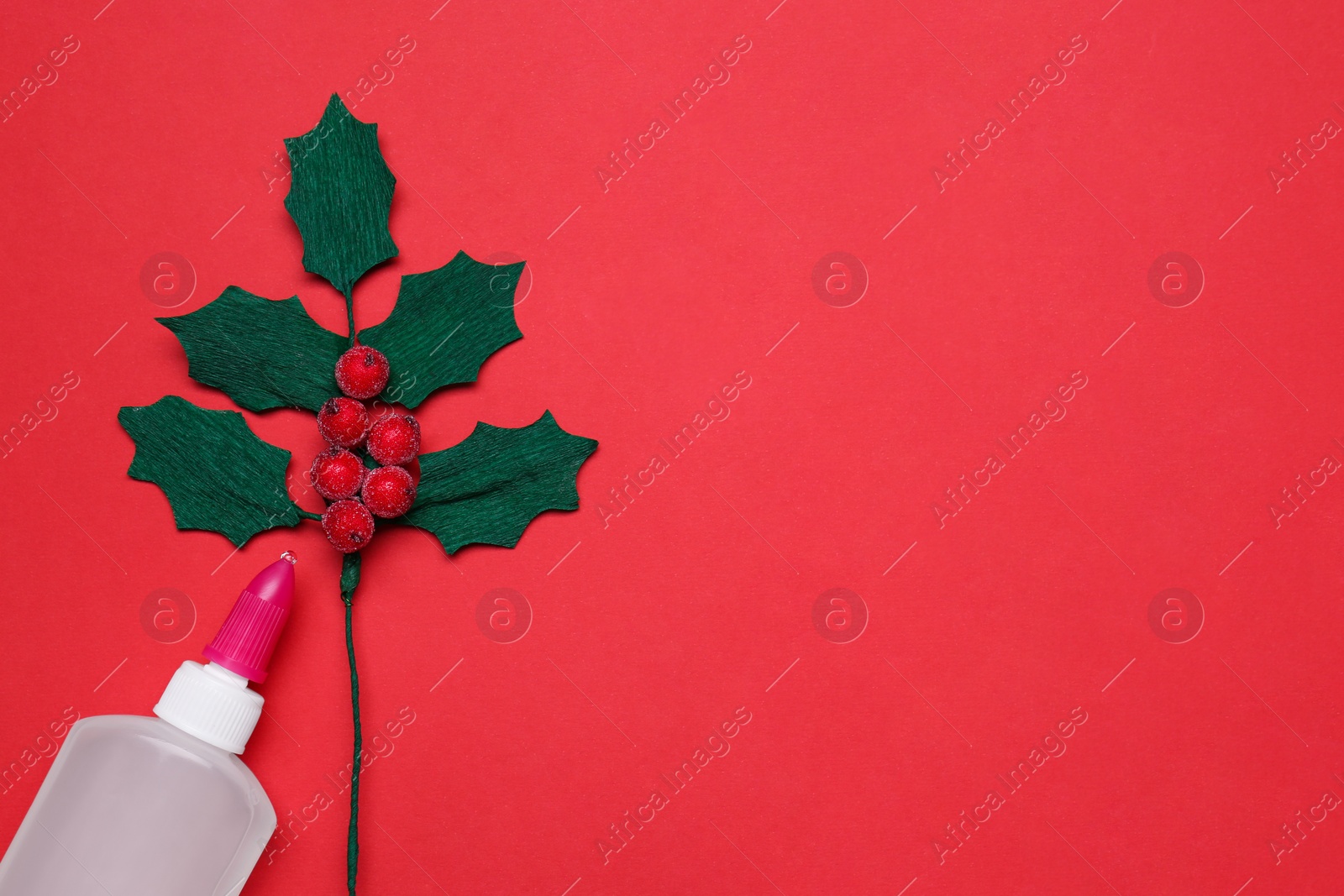 Photo of Handmade mistletoe branch and glue on red background, flat lay. Space for text