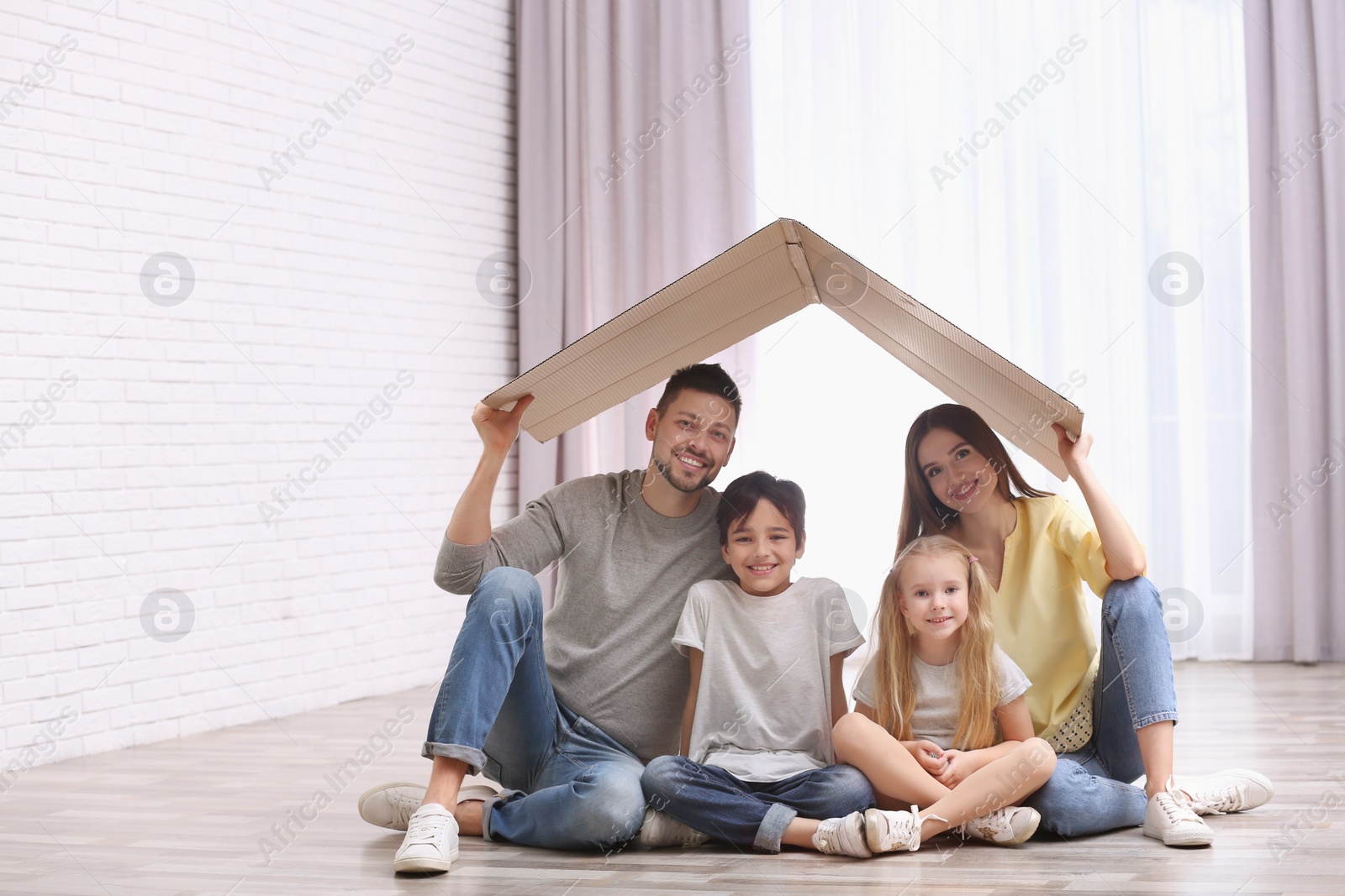 Photo of Happy family sitting under cardboard roof at home. Insurance concept