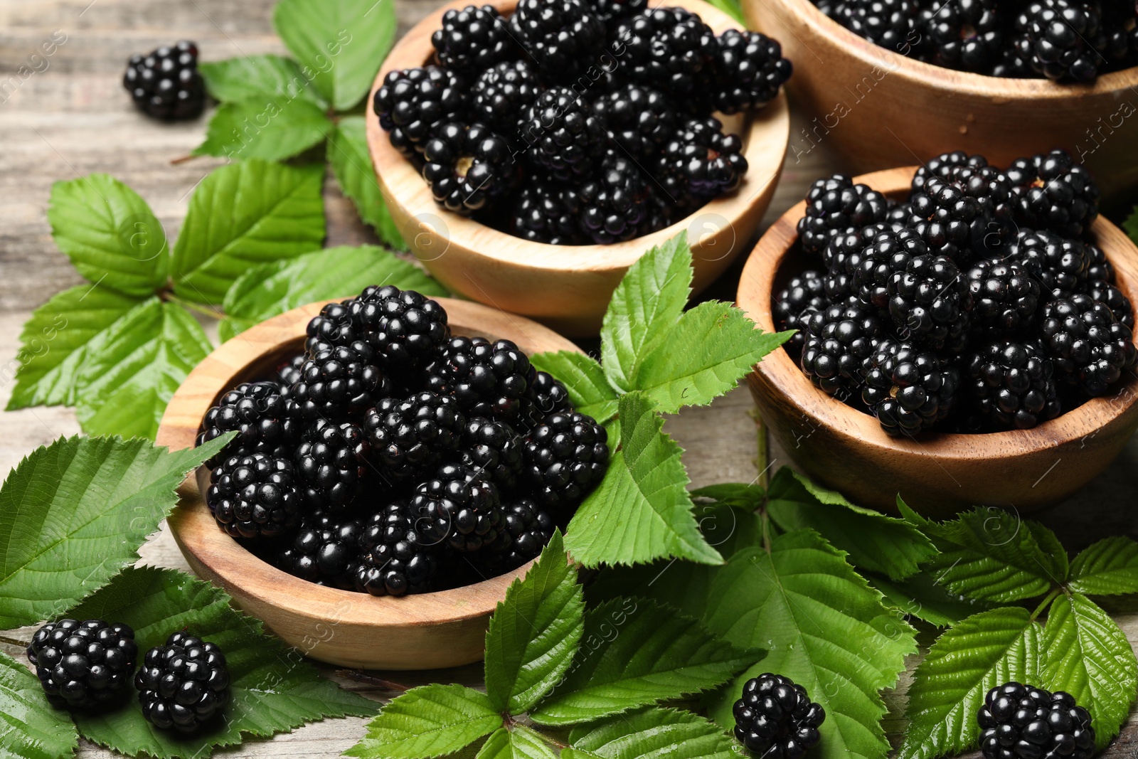 Photo of Ripe blackberries and green leaves on wooden table, closeup