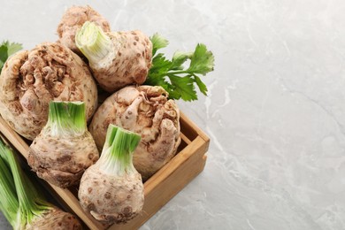 Photo of Fresh raw celery roots and wooden crate on light grey table, above view. Space for text