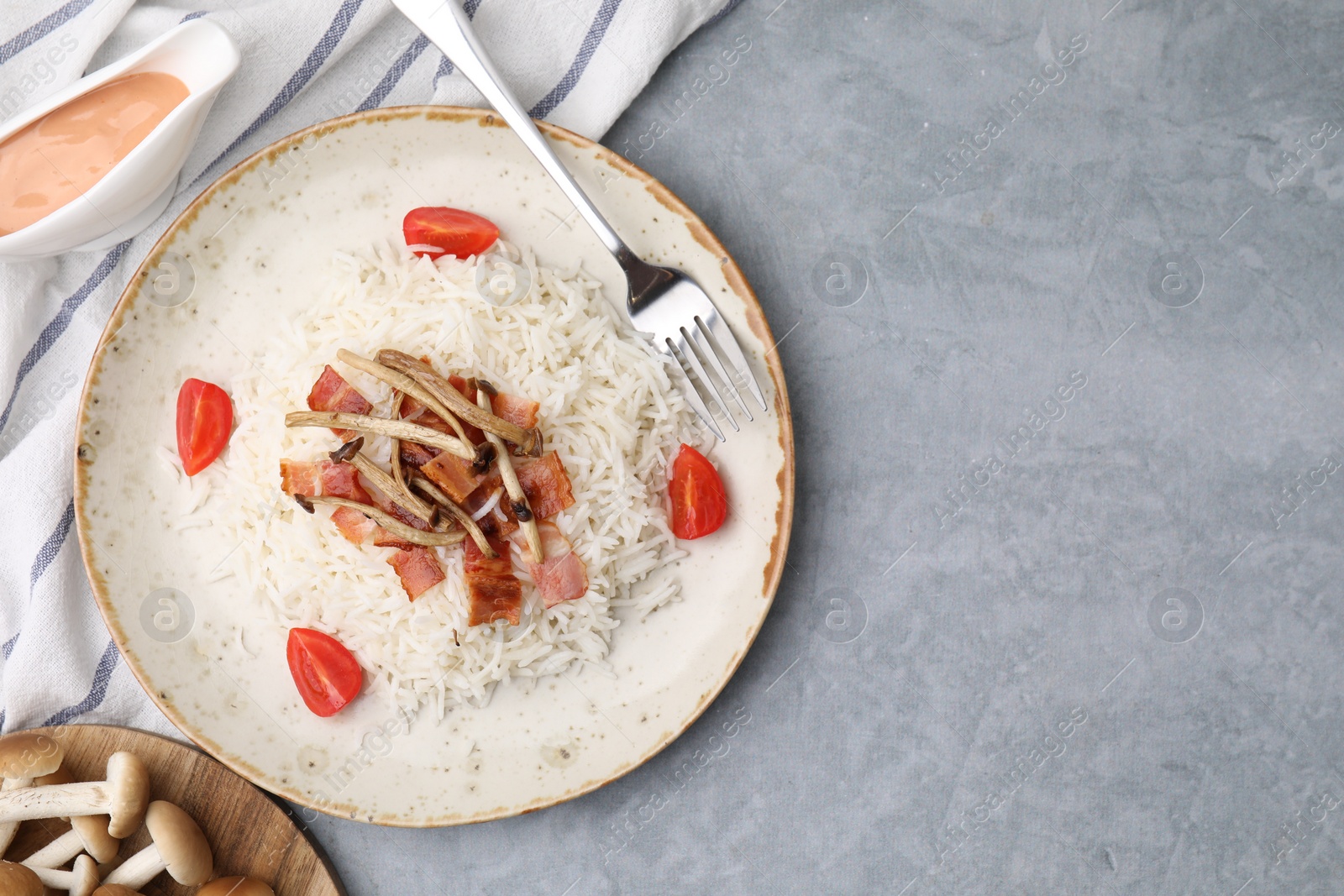 Photo of Delicious rice with bacon, mushrooms and tomatoes served on gray table, flat lay. Space for text