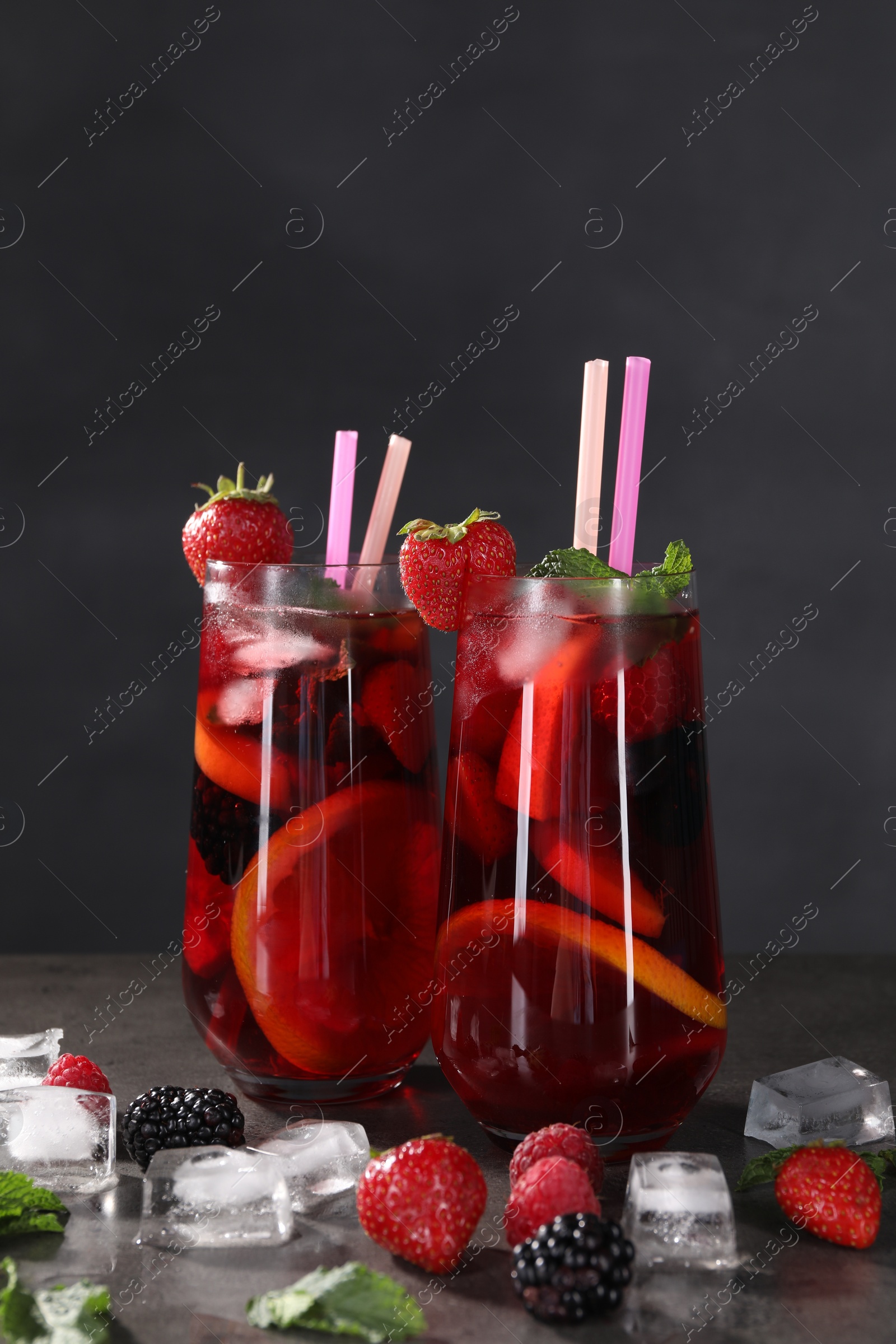 Photo of Delicious refreshing sangria, ice cubes and berries on grey table