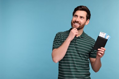 Smiling man with passport and tickets on light blue background. Space for text