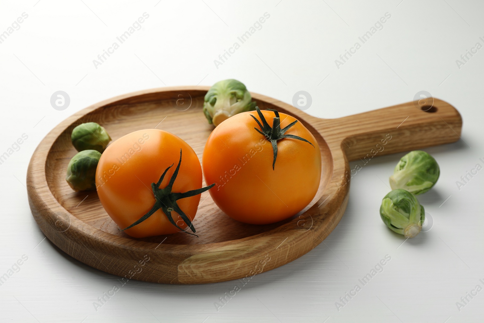 Photo of Cutting board with Brussels sprouts and tomatoes on white wooden table