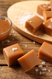 Photo of Yummy caramel candies and sea salt on wooden table, closeup