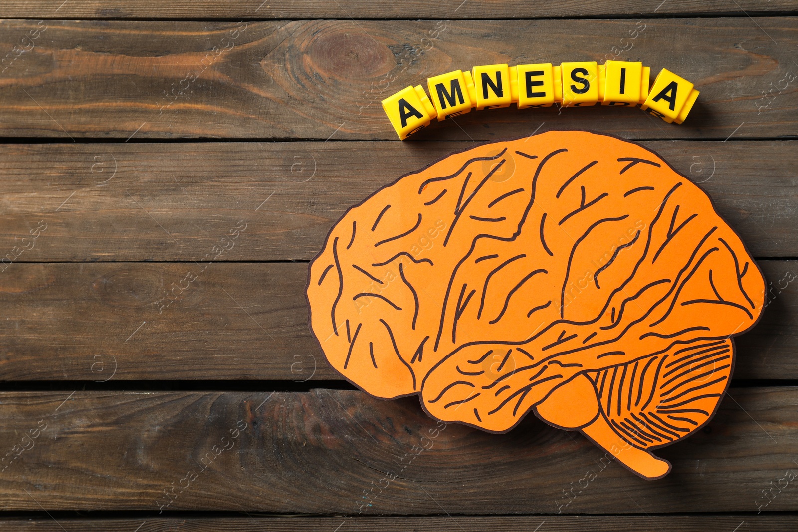 Photo of Yellow cubes with word Amnesia and paper cutout of human brain on wooden table, top view. Space for text