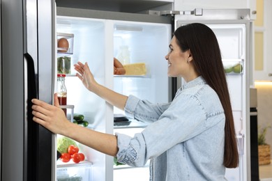 Young woman near modern refrigerator in kitchen