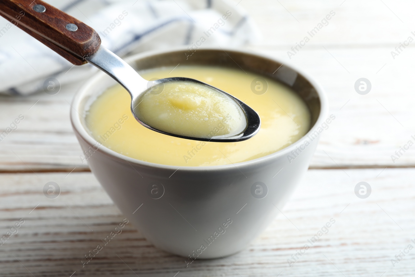Photo of Bowl and spoon of Ghee butter on white wooden table, closeup
