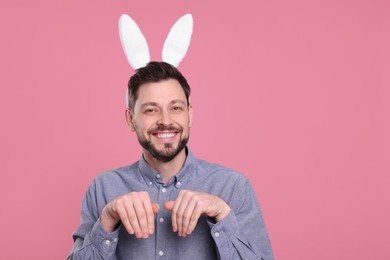 Happy man wearing bunny ears headband on pink background, space for text. Easter celebration