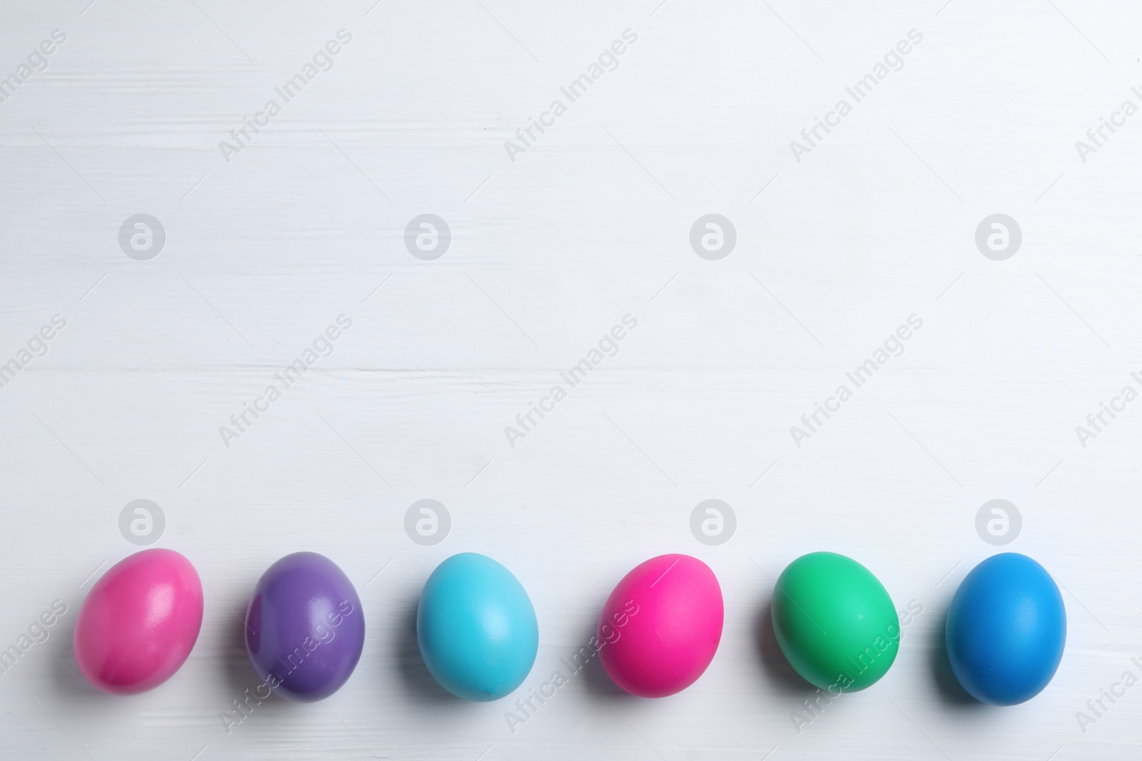 Photo of Colorful eggs on white wooden background, flat lay with space for text. Happy Easter