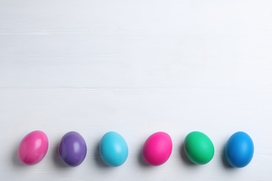 Colorful eggs on white wooden background, flat lay with space for text. Happy Easter