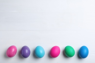 Photo of Colorful eggs on white wooden background, flat lay with space for text. Happy Easter