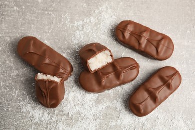 Delicious milk chocolate candy bars with coconut filling on grey table, flat lay