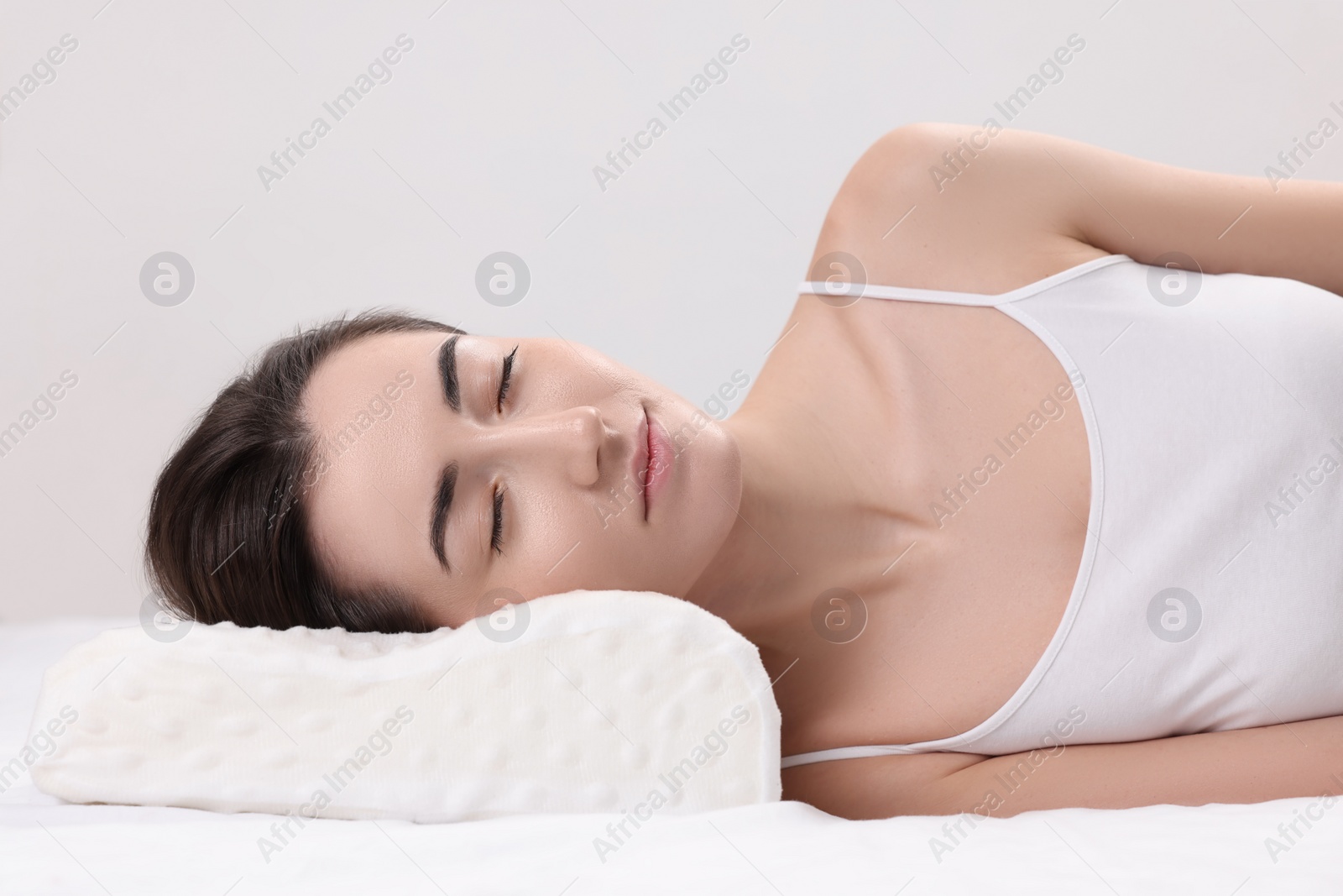 Photo of Woman sleeping on orthopedic pillow against light grey background