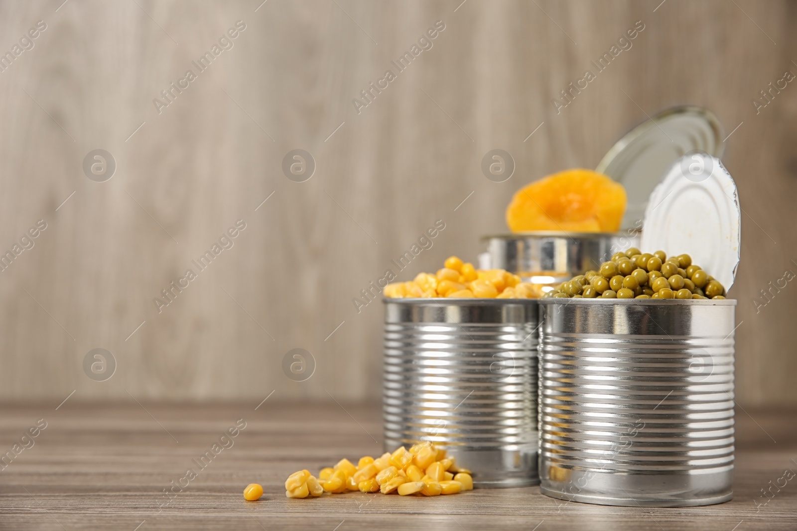 Photo of Open tin cans with conserved vegetables and fruits on wooden table. Space for text