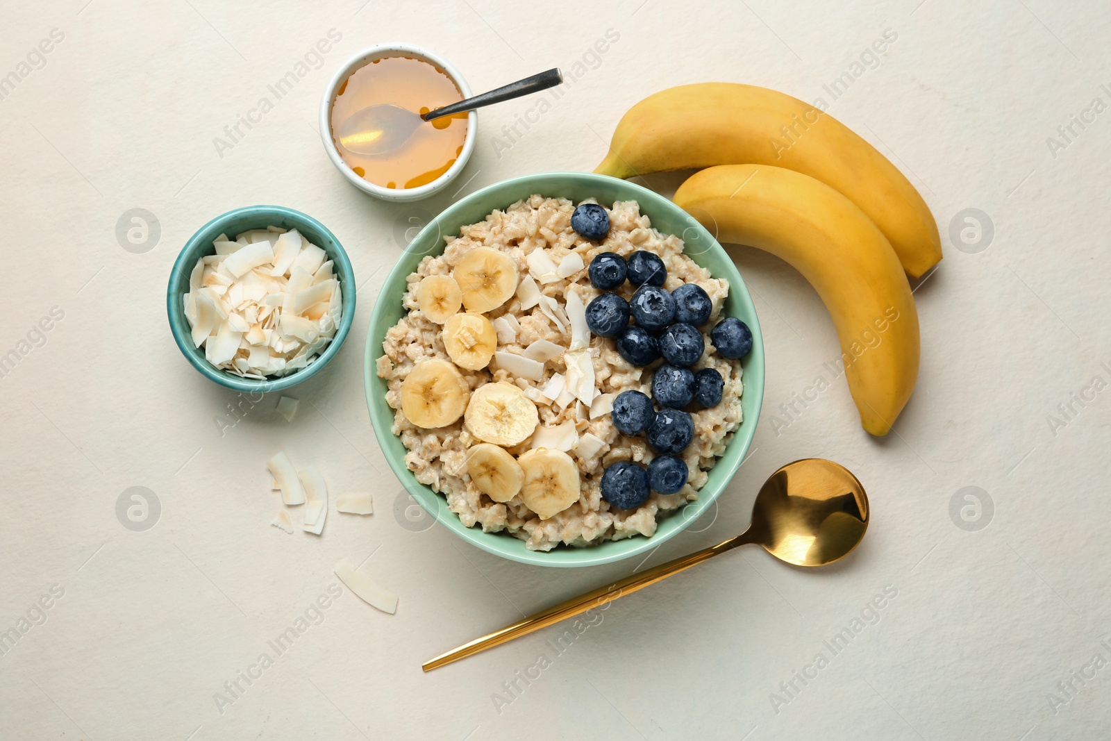 Photo of Tasty oatmeal with banana, blueberries, coconut flakes and honey served in bowl on beige table, flat lay