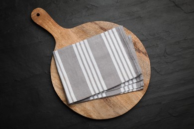 Photo of Striped kitchen towel and wooden cutting board on black table, top view