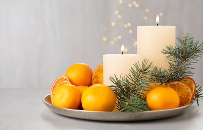 Photo of Fresh tangerines, burning candles and fir tree branches on grey table, space for text