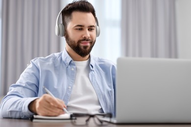 Young man in headphones watching webinar at table in room