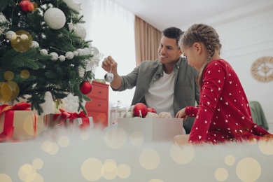 Photo of Father with his cute daughter decorating Christmas tree together at home