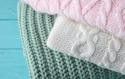 Image of Stack of folded warm sweaters on turquoise wooden background, closeup