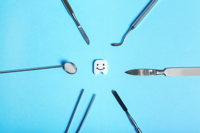 Flat lay composition with professional dental tools and small plastic tooth on color background