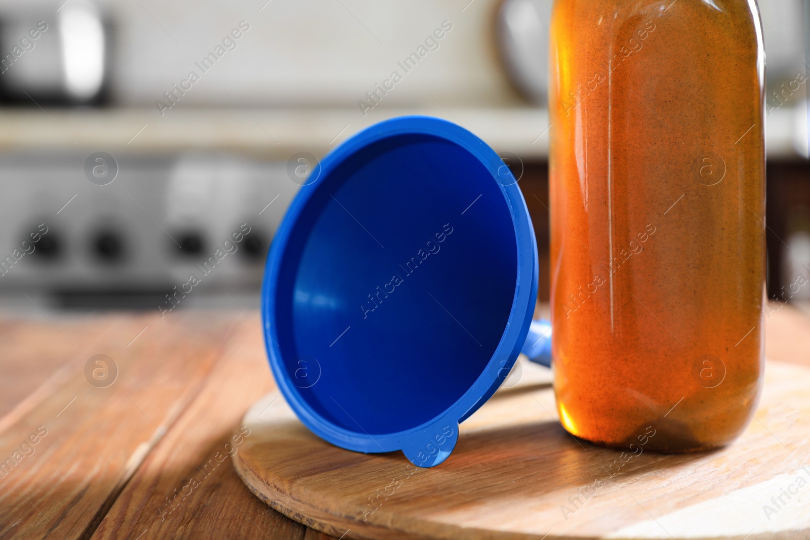 Photo of Bottle with used cooking oil and funnel on wooden table in kitchen, closeup