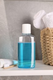 Photo of Bottle of mouthwash, toothpaste, toothbrush and towels on shelf in bathroom