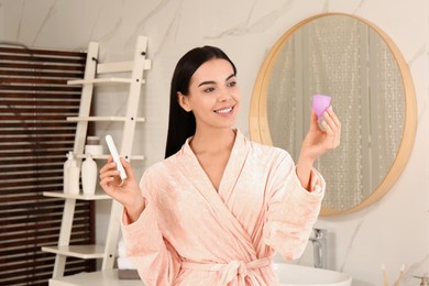 Photo of Young woman with menstrual cup and tampon in bathroom