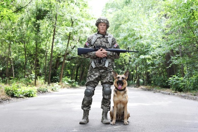 Photo of Man in military uniform with German shepherd dog, outdoors