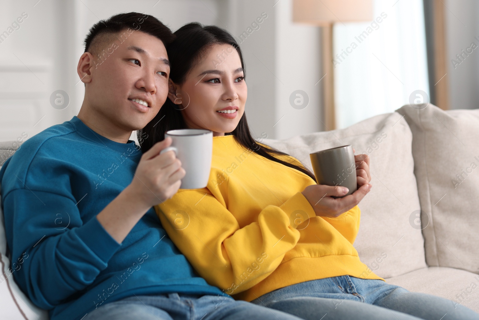 Photo of Happy couple with cups of drink on sofa at home