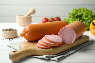 Photo of Board with tasty boiled sausages on white wooden table, closeup