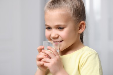 Photo of Little girl drinking fresh water from glass indoors