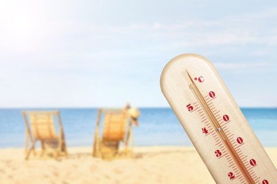 Image of Weather thermometer and beautiful sandy beach with wooden sunbeds on background. Heat stroke warning