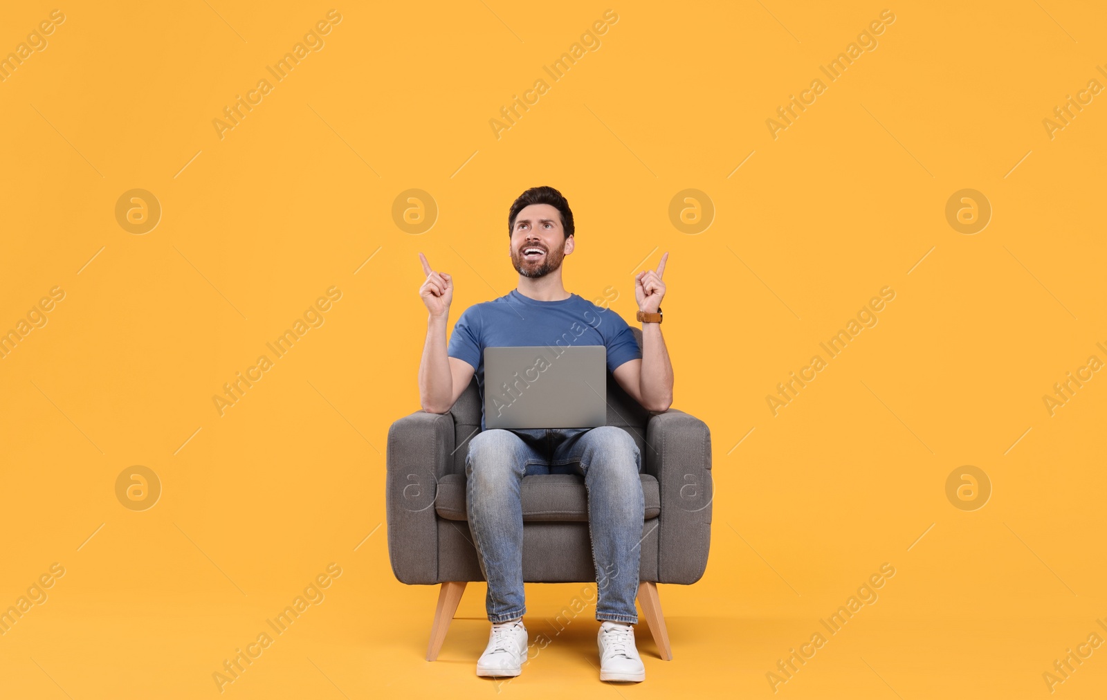 Photo of Emotional man with laptop sitting in armchair against yellow background