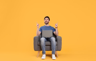 Emotional man with laptop sitting in armchair against yellow background