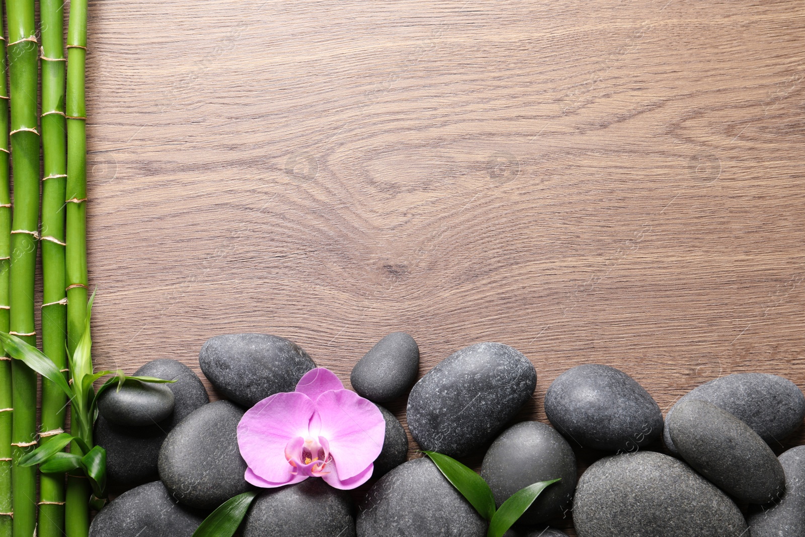 Photo of Spa stones, beautiful orchid flower and bamboo stems on wooden table, flat lay. Space for text