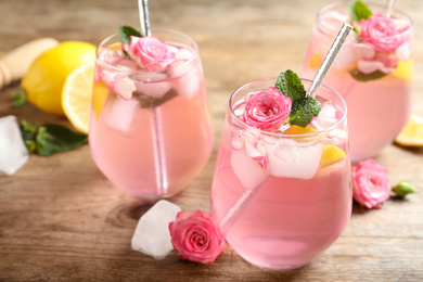 Delicious refreshing drink with rose flowers and lemon slices on wooden table, closeup