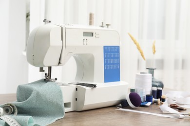 Photo of White sewing machine, cloth and craft accessories on wooden table indoors