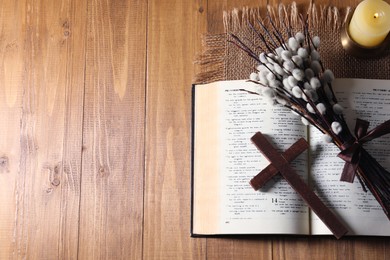 Photo of Cross, Bible, burning candle and willow branches on wooden table, flat lay. Space for text